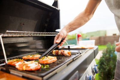 Personne cuisant des viandes sur un barbecue de jardin au gaz.